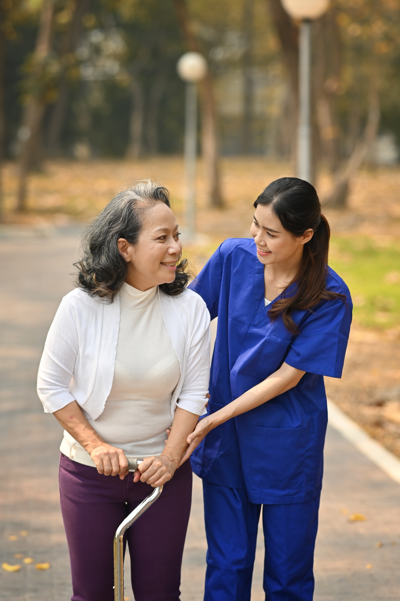 Careful caregiver taking care of elderly woman patient during walking outdoor.