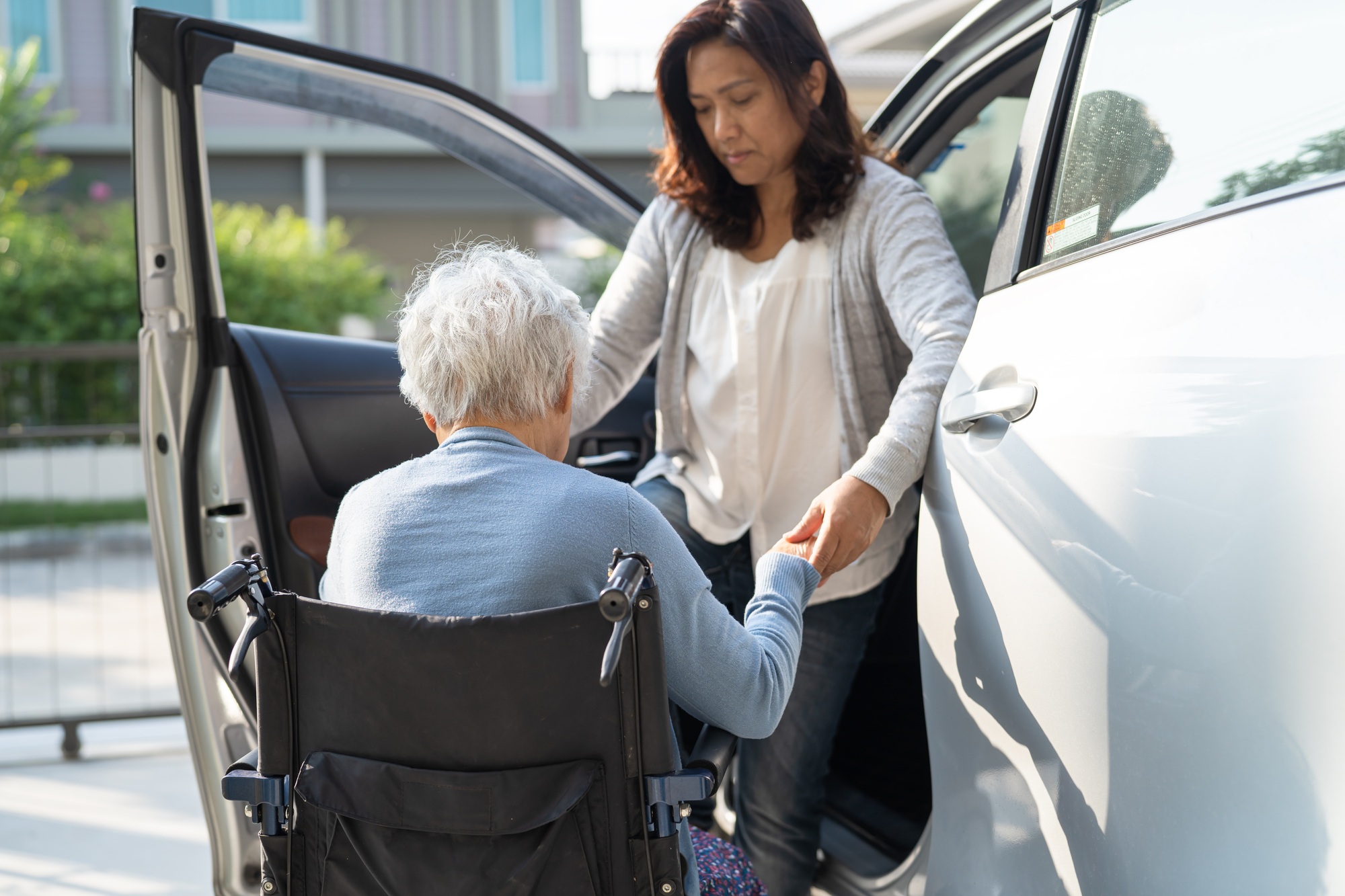 Caregiver daughter help and support asian senior woman patient prepare get to her car.